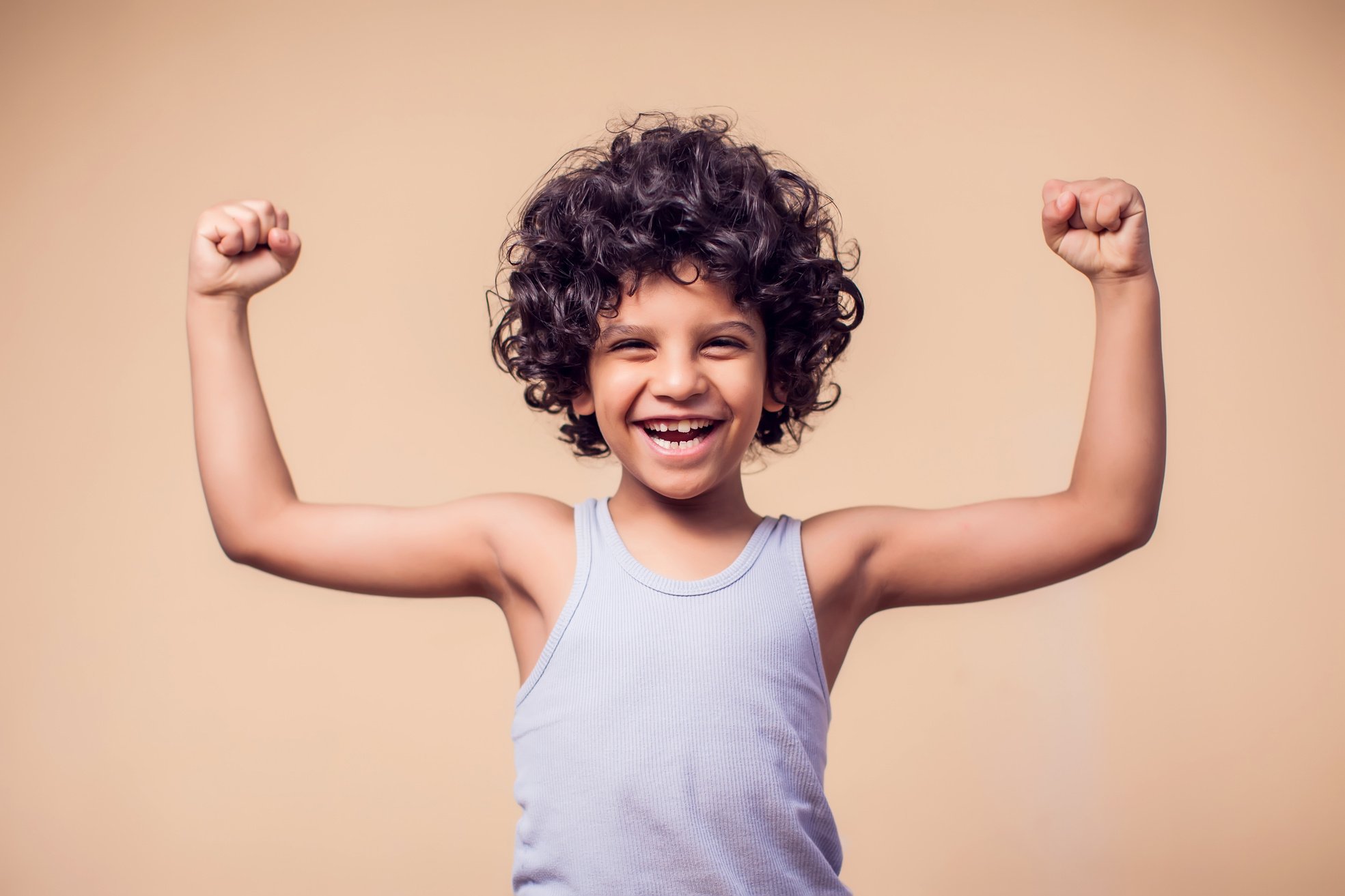 A portrait of smiling kid boy with curly hair showing strong. Children and health concept